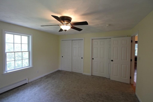 unfurnished bedroom with baseboard heating, multiple windows, and two closets