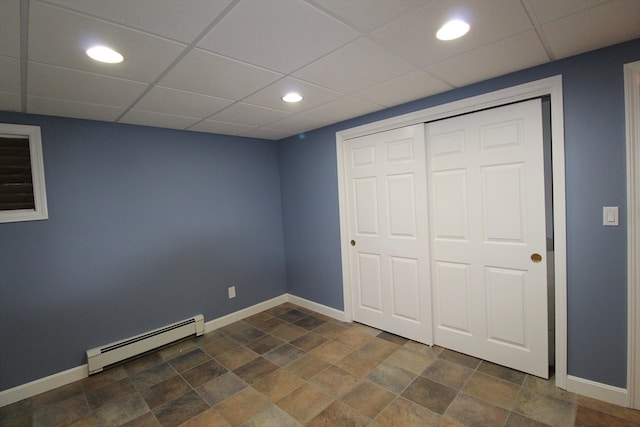 unfurnished bedroom featuring a baseboard radiator, a closet, and a drop ceiling