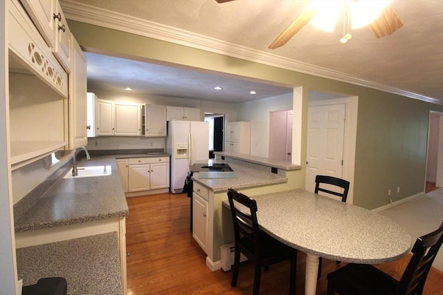 kitchen with white fridge with ice dispenser, a kitchen breakfast bar, ornamental molding, a sink, and light wood finished floors