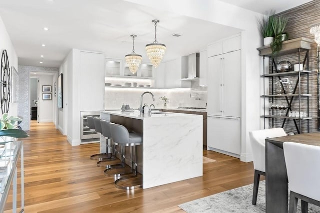 300 Blvd 3I, Boston, MA 02210 - kitchen featuring wall chimney exhaust hood, a chandelier, white cabinets, an island with sink, and light wood finished floors