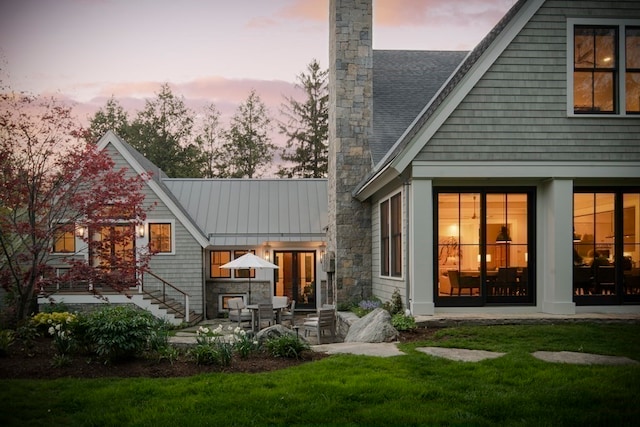 back house at dusk featuring a patio area and a lawn