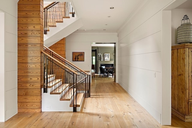 hallway featuring crown molding, light hardwood / wood-style floors, and wooden walls