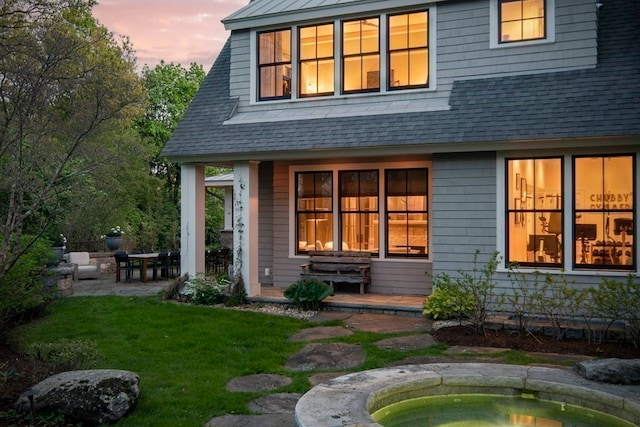 back house at dusk with a patio area, a lawn, and a hot tub