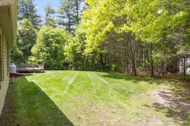 view of grassy yard featuring a deck and a view of trees