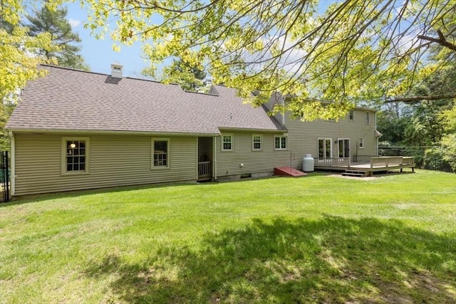 rear view of property with a deck, a lawn, and a shingled roof