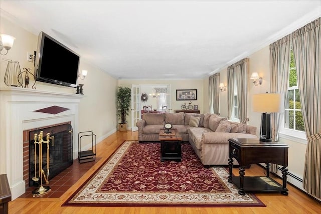 living room with healthy amount of natural light, a fireplace with flush hearth, crown molding, wood finished floors, and baseboards
