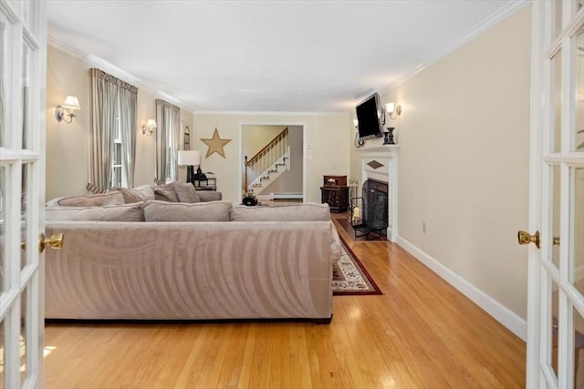 living area with light wood-type flooring, stairway, ornamental molding, french doors, and a fireplace with flush hearth