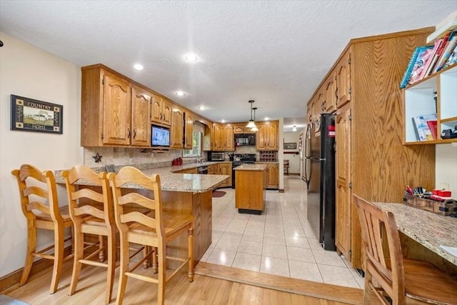 kitchen featuring black appliances, a peninsula, brown cabinetry, a breakfast bar area, and a textured ceiling