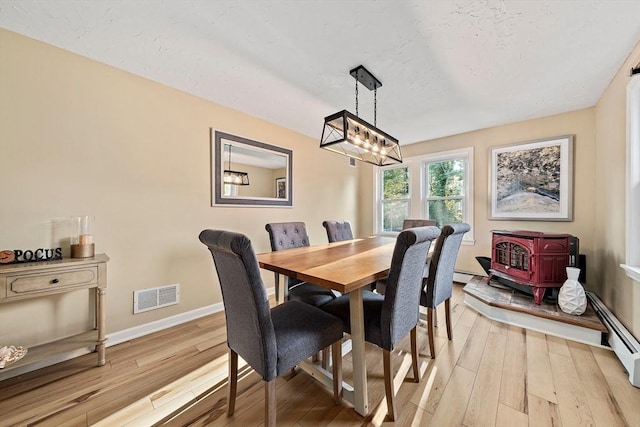 dining space featuring visible vents, baseboard heating, a wood stove, light wood-type flooring, and baseboards