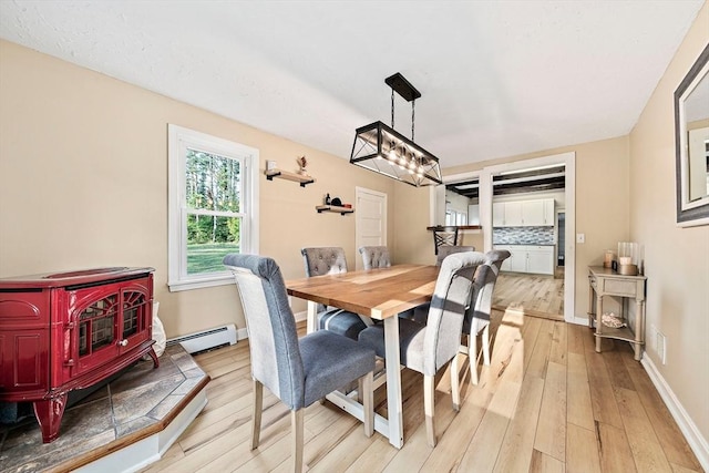 dining room featuring an inviting chandelier, a baseboard radiator, a wood stove, and light wood-type flooring