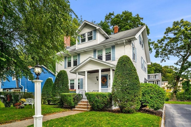 traditional style home with covered porch, a front lawn, and a chimney