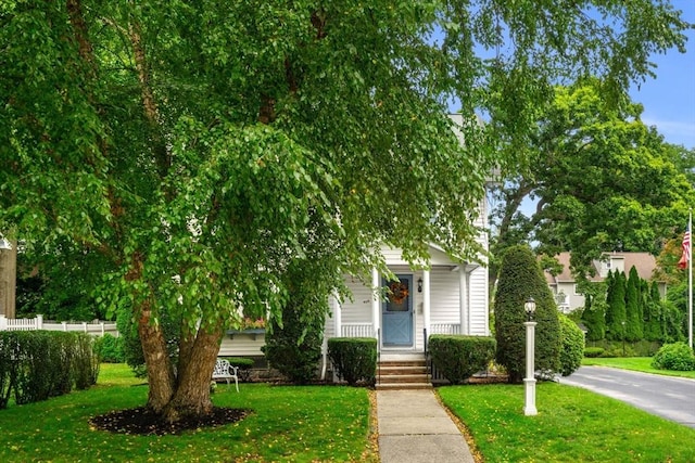 view of property hidden behind natural elements with covered porch, fence, and a front lawn