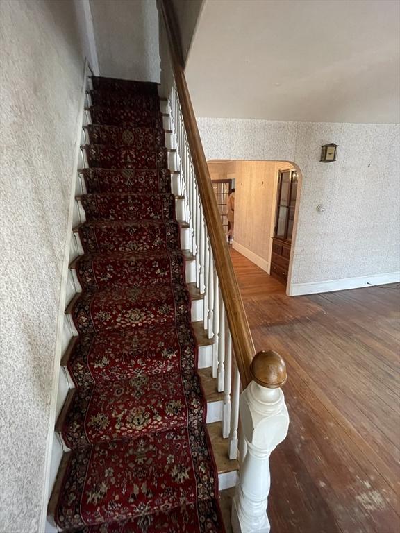 staircase featuring wood finished floors, wallpapered walls, arched walkways, and baseboards