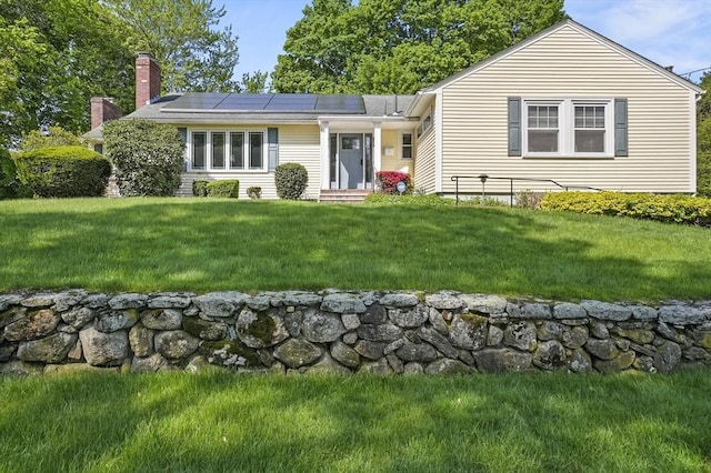view of front facade with a chimney, solar panels, and a front yard