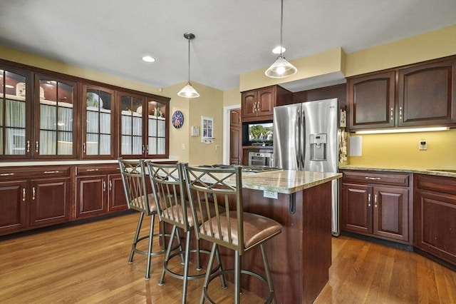 kitchen featuring wood finished floors, a breakfast bar area, a kitchen island, hanging light fixtures, and stainless steel refrigerator with ice dispenser