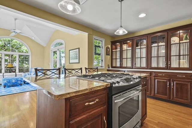 kitchen with stainless steel range with gas stovetop, light wood-type flooring, healthy amount of natural light, vaulted ceiling, and pendant lighting