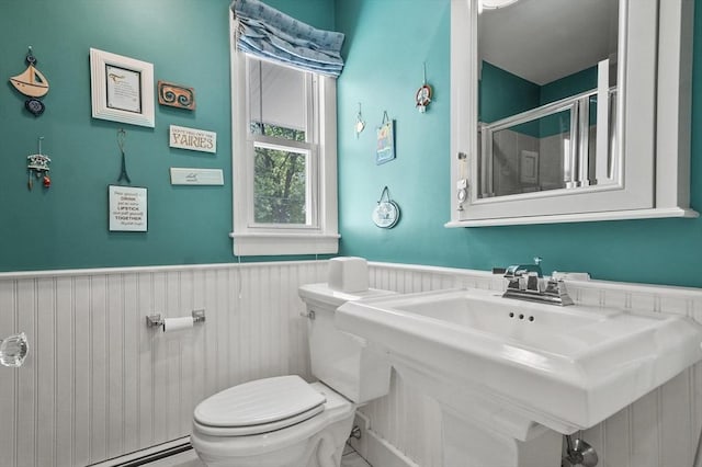 bathroom featuring wainscoting, toilet, a shower stall, a baseboard heating unit, and a sink