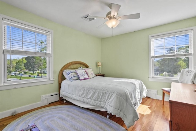 bedroom with multiple windows, wood finished floors, and a baseboard heating unit