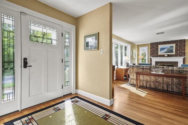 foyer entrance with wood finished floors, baseboards, and a brick fireplace