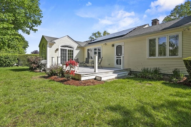 back of property featuring roof mounted solar panels, a deck, a lawn, a chimney, and a shingled roof