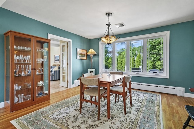 dining space featuring a baseboard heating unit, baseboards, wood finished floors, and a chandelier