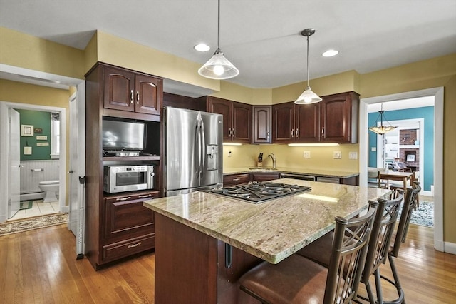 kitchen with appliances with stainless steel finishes, light stone counters, light wood-style flooring, a kitchen island, and recessed lighting