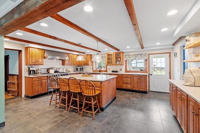 kitchen with wall chimney range hood, high end range, a kitchen island, sink, and a kitchen breakfast bar