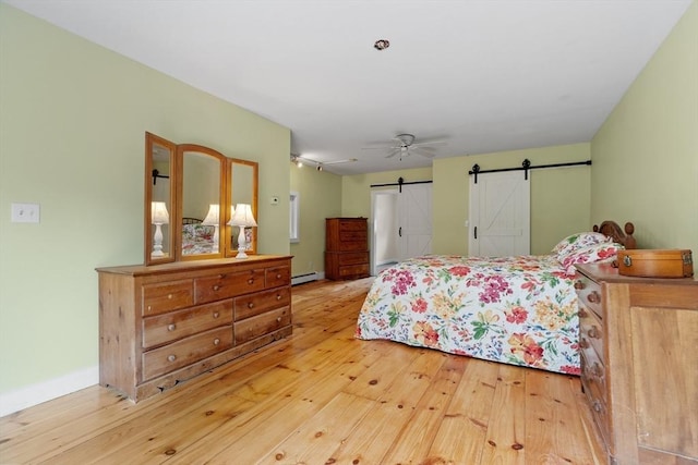 bedroom with ceiling fan, a baseboard radiator, a barn door, and light wood-type flooring