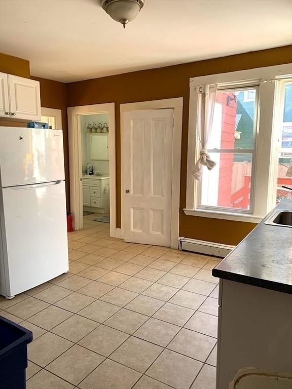 6-8 Imrie Rd, Boston, MA 02134 - kitchen featuring freestanding refrigerator, a baseboard radiator, light tile patterned floors, white cabinetry, and healthy amount of natural light