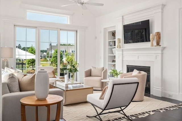 living room featuring light wood-type flooring, a high end fireplace, ceiling fan, and baseboards