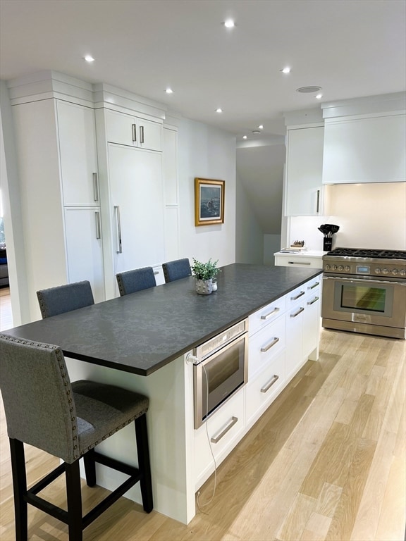 kitchen featuring a breakfast bar area, white cabinetry, light wood-type flooring, and appliances with stainless steel finishes