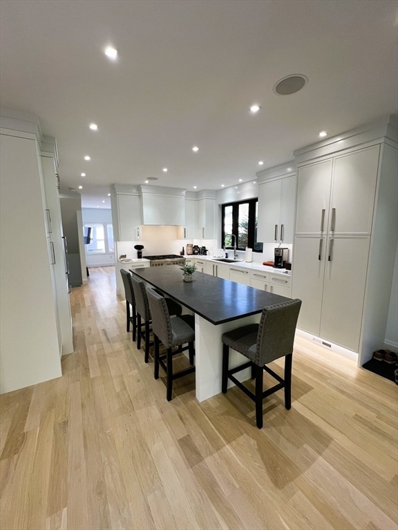 kitchen with white cabinetry, sink, a kitchen bar, a center island, and light wood-type flooring