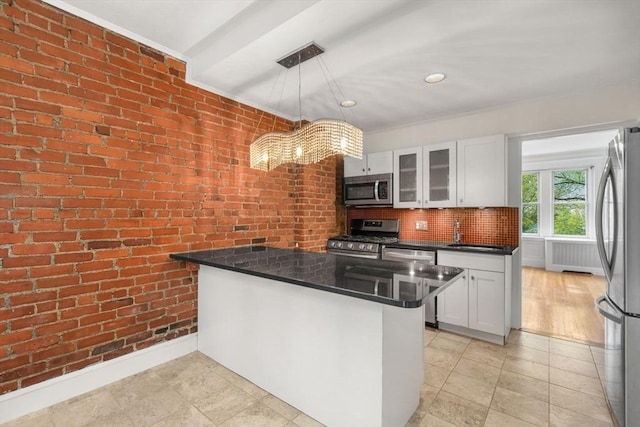 kitchen with glass insert cabinets, brick wall, white cabinetry, a peninsula, and stainless steel appliances