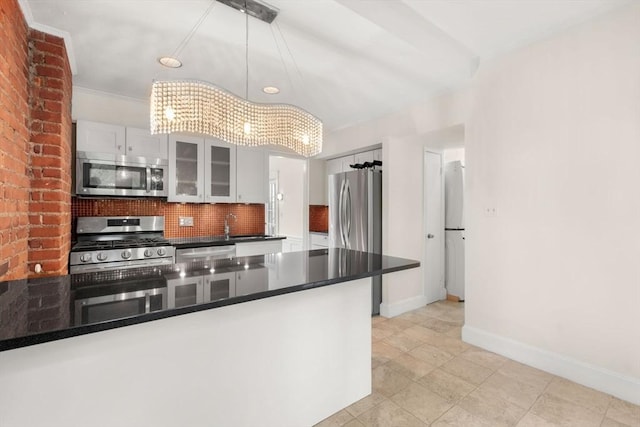 kitchen with dark countertops, stainless steel appliances, a notable chandelier, white cabinets, and decorative backsplash