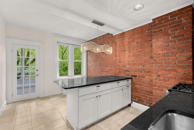 kitchen featuring brick wall, light tile patterned flooring, white cabinetry, and dark countertops