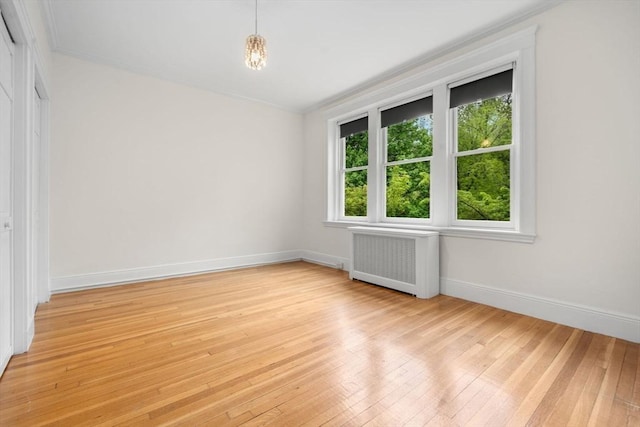 unfurnished room featuring crown molding, light wood-style flooring, baseboards, and radiator heating unit