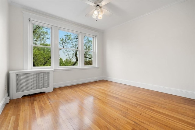 spare room with a ceiling fan, light wood-style flooring, baseboards, radiator heating unit, and crown molding