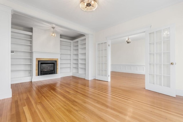 unfurnished living room with an inviting chandelier, light wood-style flooring, a fireplace, and built in shelves