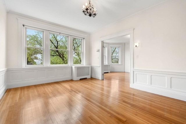 interior space featuring radiator, a wainscoted wall, ornamental molding, an inviting chandelier, and light wood finished floors
