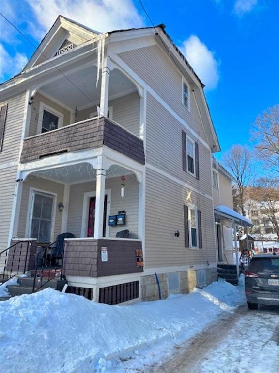 snow covered property featuring a porch and a balcony