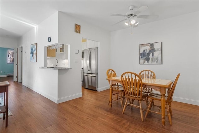 dining area featuring a baseboard heating unit, a ceiling fan, baseboards, and wood finished floors