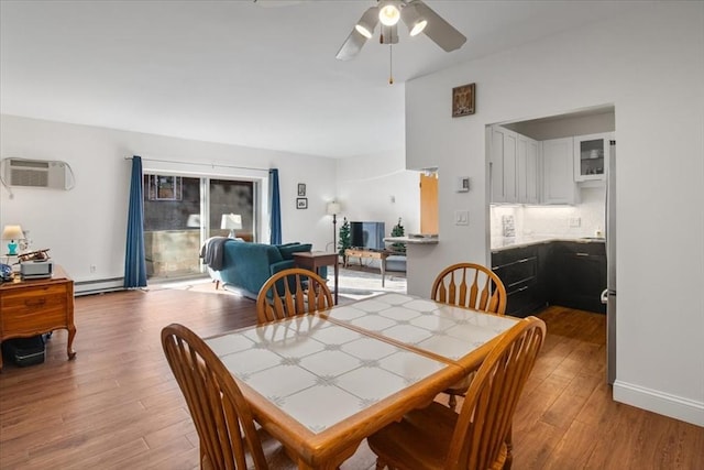 dining area with a baseboard radiator, light wood-style flooring, a wall unit AC, and a ceiling fan