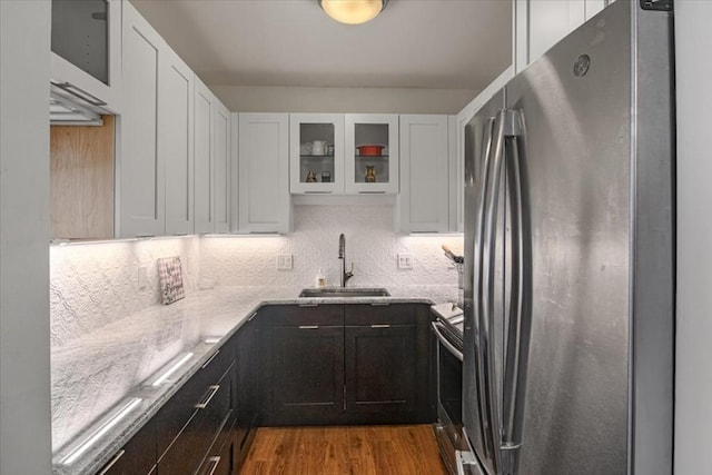 kitchen featuring stainless steel appliances, glass insert cabinets, a sink, and light stone countertops