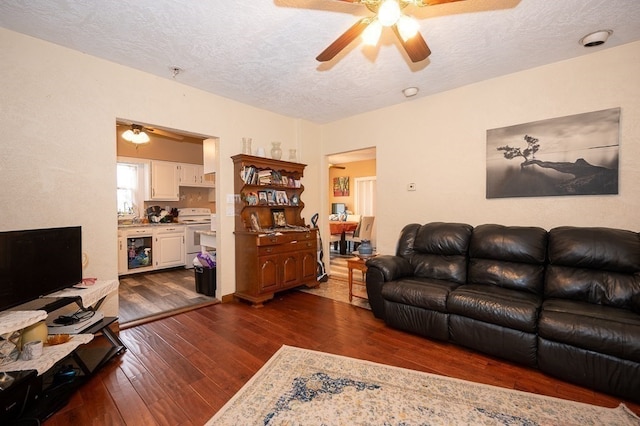 living room with dark wood-type flooring, a textured ceiling, and ceiling fan