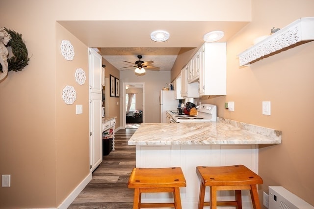 kitchen with white cabinets, kitchen peninsula, white appliances, a kitchen breakfast bar, and dark hardwood / wood-style floors