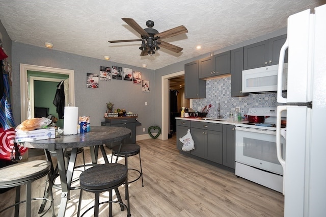 kitchen featuring gray cabinets, light wood-type flooring, a textured ceiling, and white appliances