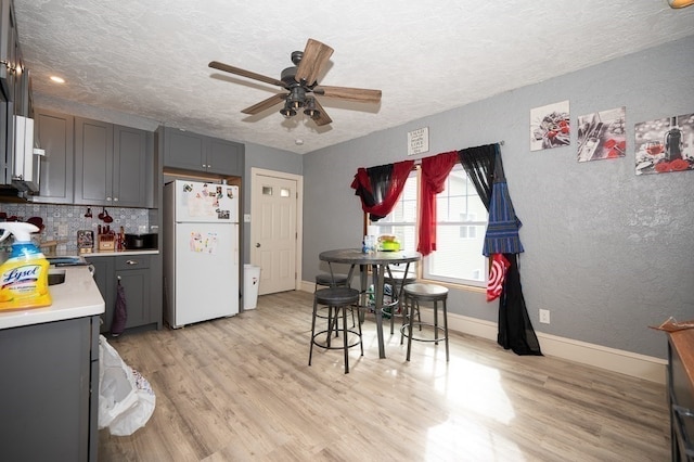 kitchen featuring ceiling fan, light hardwood / wood-style flooring, backsplash, gray cabinets, and white fridge