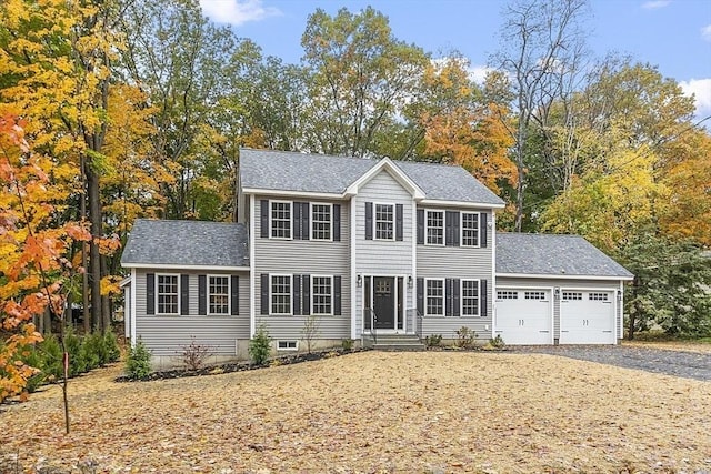 colonial house with driveway, an attached garage, and a shingled roof