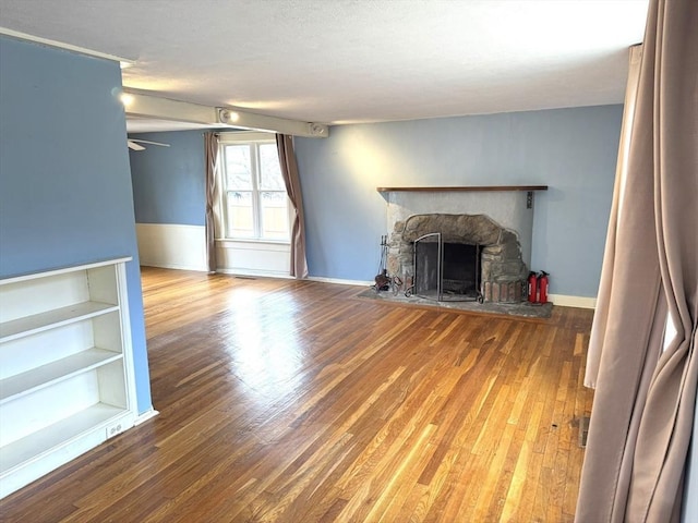 unfurnished living room featuring wood finished floors, baseboards, and a stone fireplace