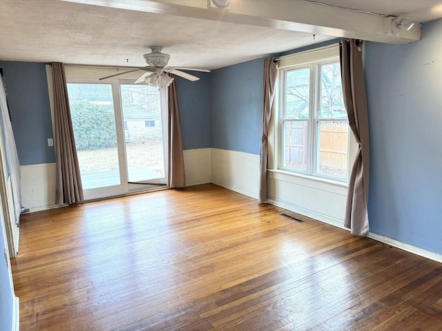 unfurnished room with a ceiling fan, hardwood / wood-style floors, wainscoting, and a healthy amount of sunlight